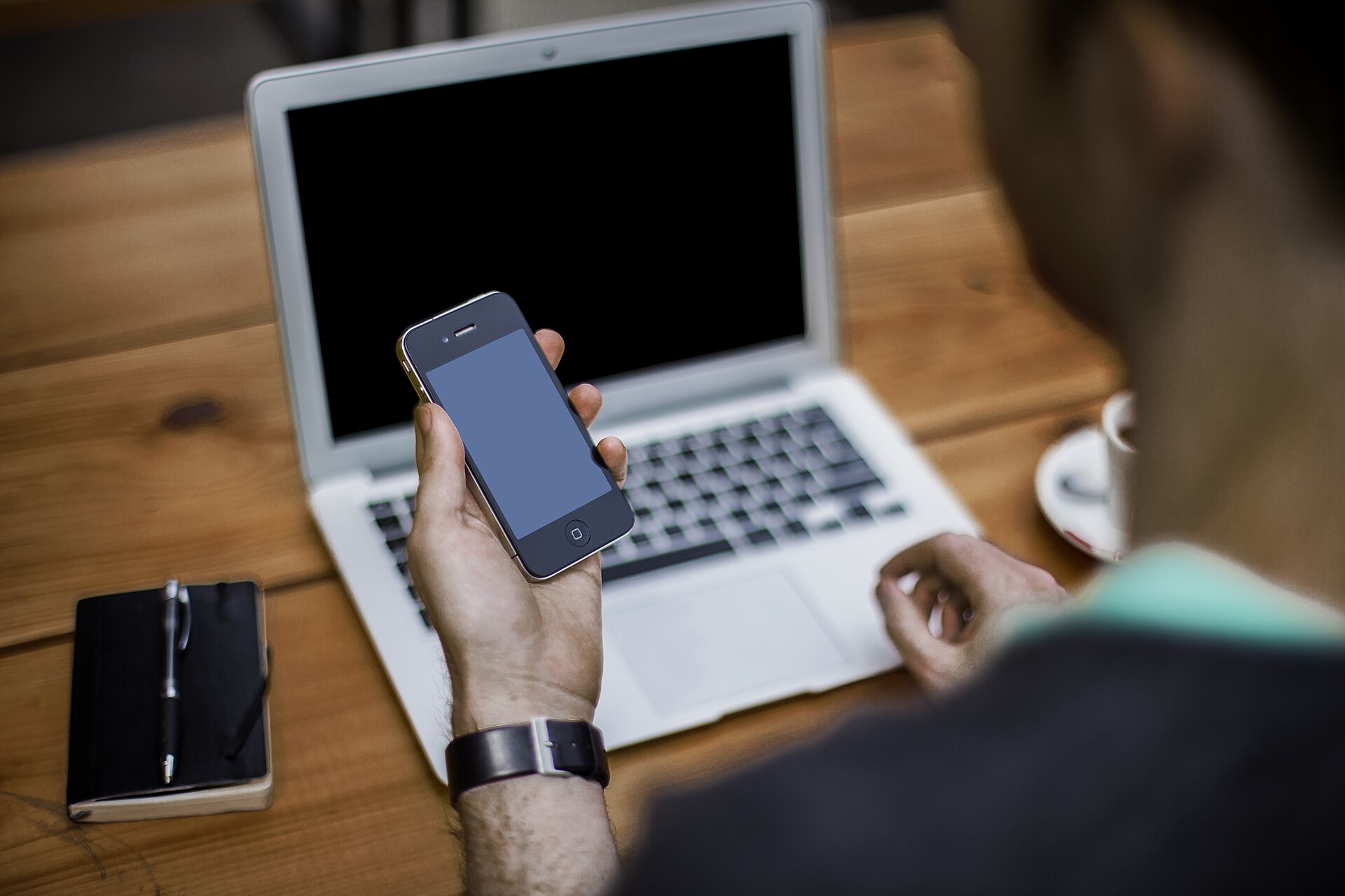 A person holding a smartphone next to a laptop